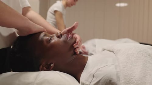 African American Woman Receiving Relaxing Facial Massage at Spa