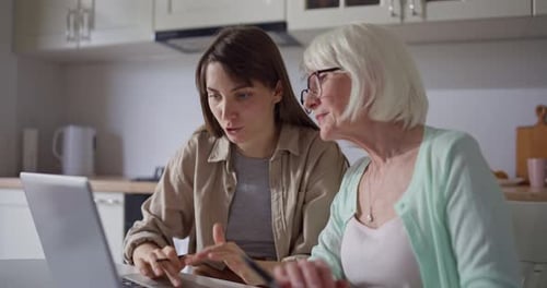 Woman Helping Senior with Laptop Computer in Kitchen