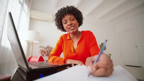 Woman Video Conferencing and Writing at Desk