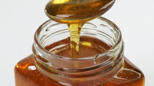 A Metal Spoon Is Dipped To Take Honey In A Jar On The White Background