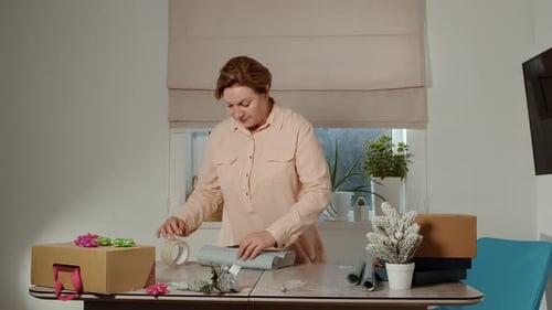 Woman wrapping Christmas presents at a table indoors