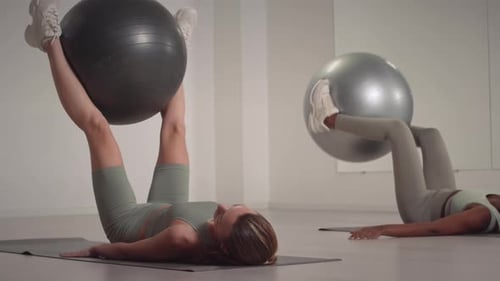 Two Diverse Women Lifting Fit Ball during Indoor Workout