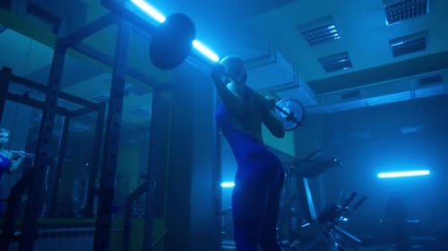 Side View of Dark Silhouette of Woman with Slender Body is Squatting with Barbell in Dark Gym with