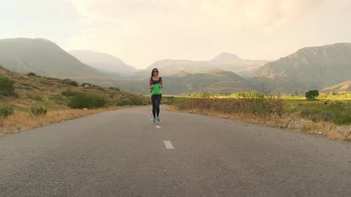 Young Woman Runs on a Paved Road Through Mountains Golden Light on the Valley