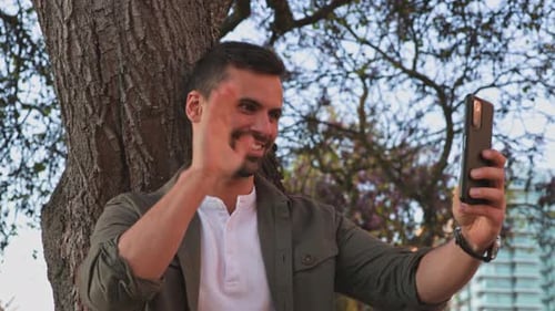 A Handsome and Happy Businessman Gives a Video Call on His Friend's Smartphone and Shows a Greeting