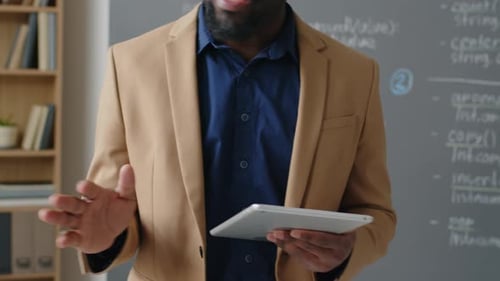 Bearded man teaches in front of chalkboard with tablet