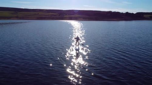 4K aerial arc shot of a paddle boarder on a lake during the evening.