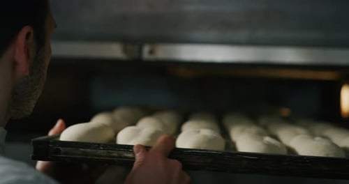 Slow motion close up of a baker pulling into the oven balls of dough covered with wheat flour read