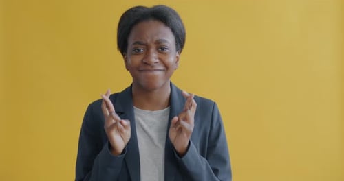 Portrait of Hopeful Young African American Woman Crossing Fingers Making Wish and Smiling
