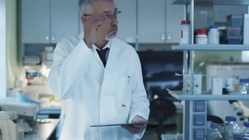 Senior scientist is walking with a tablet in a laboratory where colleagues are working.