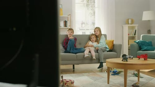 Two Cute Little Girls and Young Adorable Boy Watching Television While Sitting on a Sofa. Happy Kid