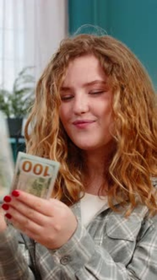 Woman Sits on Sofa Excitedly Counting Cash Dollars Celebrating Lottery Win or Unexpected Income Joy