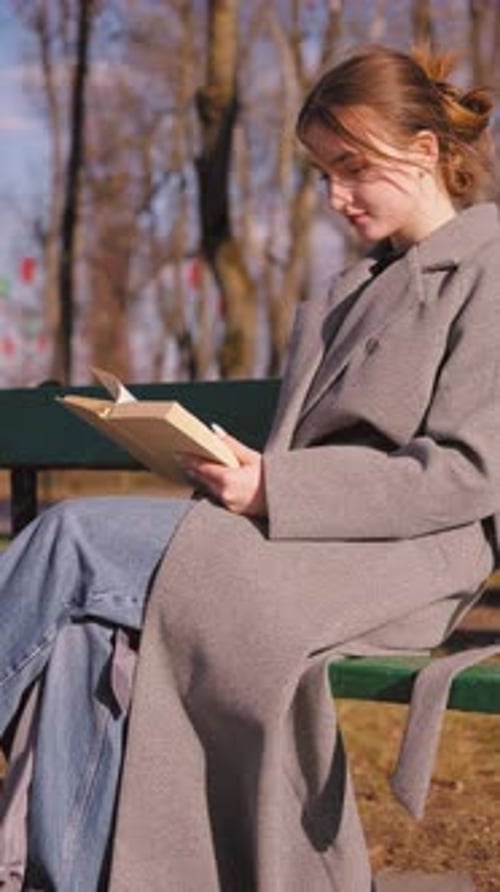 Young woman reading a book on a bench in a park