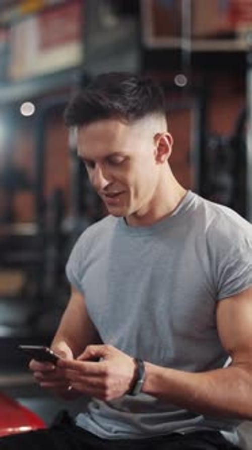 A Man is Actively Using His Smartphone While Engaging in a Workout at the Gym Facility