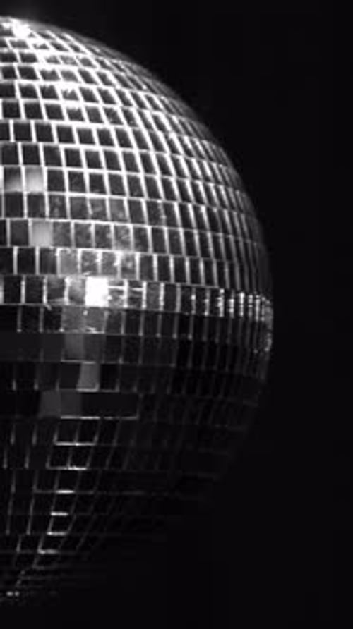 Elegant silver disco ball spinning in dim light. Vertical