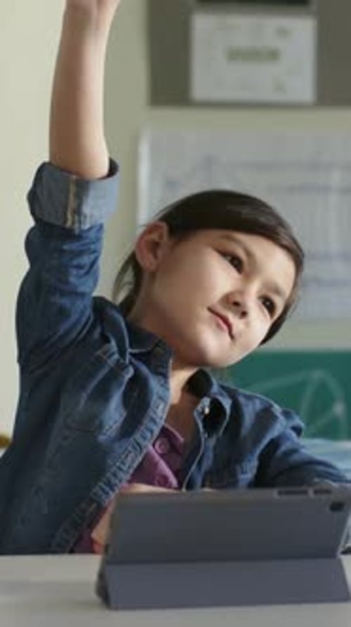 Vertical video: Teacher asking kid raising right arm, left to chest, talking in class with tablet