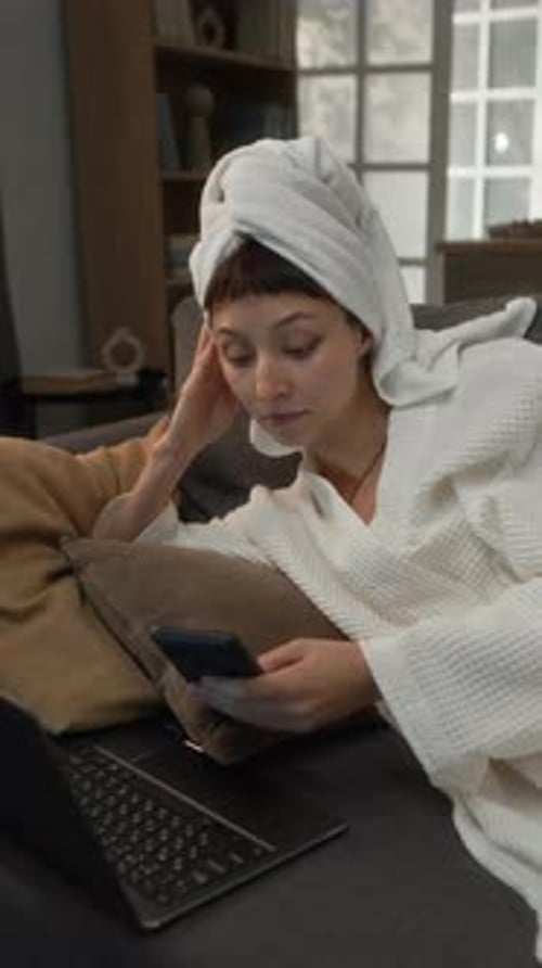 Woman in bathrobe using phone on couch indoors
