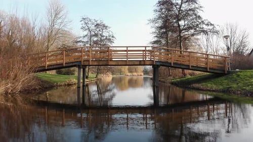 AERIAL: flying low above the water going under the bridge into the park during winter time