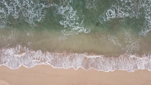 Stable Aerial top view over clear, Turquoise ocean water foaming at the shore, washing the golden sa