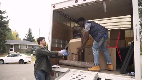 Men unload boxes from moving truck in suburb