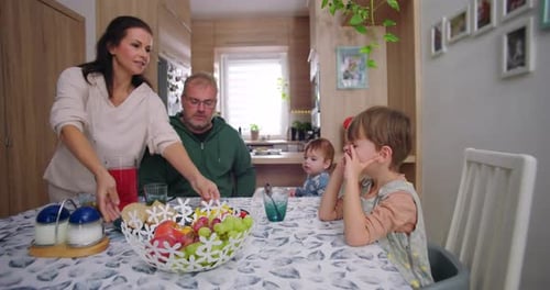 Family gathering at dining table, mother serving plates of food for breakfast while father and
