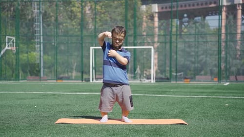 Dwarf young man exercising in the park doing body stretches with his arms.