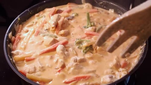 Creamy curried chicken, vegetables meal stirred in hot pan with fork