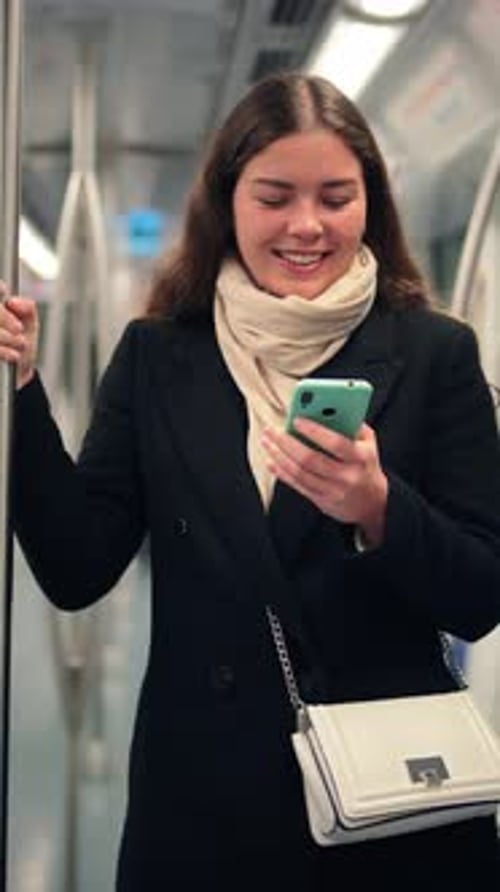 Focused Young Woman Using Her Smartphone While Traveling on the Subway Holding Onto the Pole with