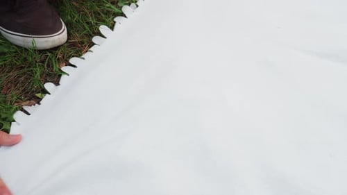 Young Man Stretching White Cloth On Grass With Hands