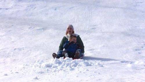 Mutter und Sohn genießen Winterspaß beim Rodeln in Zeitlupe einen verschneiten Hügel hinunter