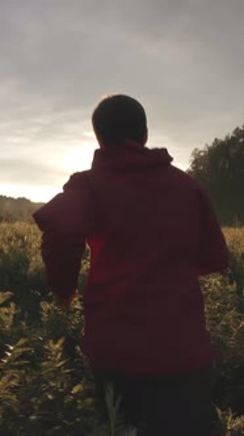 Vue depuis le dos d'un homme en veste rouge et jean qui court sur le terrain vert près des conifères