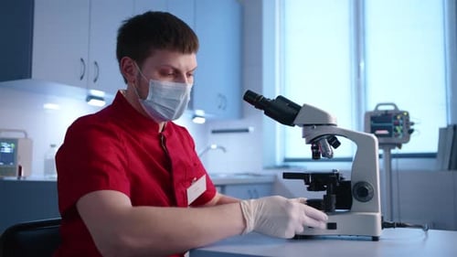 Veterinario joven masculino centrado en la investigación de laboratorio con un microscopio binocular