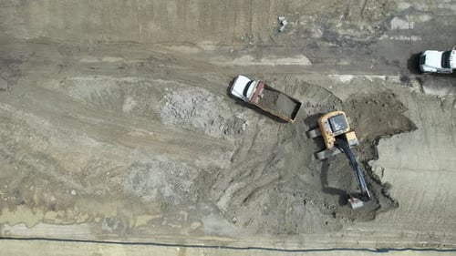 Aerial view of an excavator loads a dump truck with sand at a construction site.