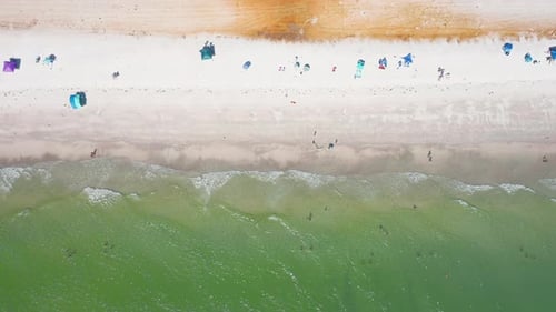 Top-down view of sandy shoreline with beach umbrellas and turquoise waves