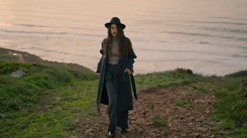 Energetic Young Lady Walking Coast in Stylish Coat with Beautiful Ocean Backdrop