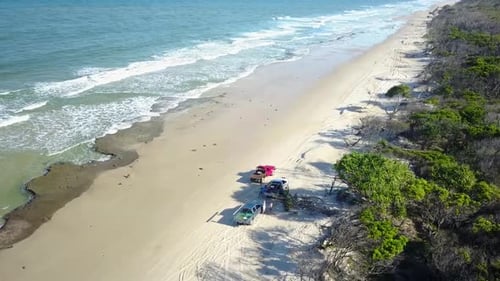 Aerial orbit Drone shot flying around cars on a Australian white sand beach, waves hiting the coast,