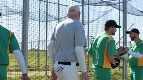Nodding coach guiding three players through batting cage, practicing bat swings to start next drill
