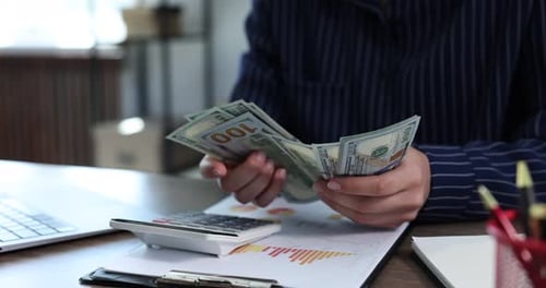 Counting Money at Desk with Calculator and Charts