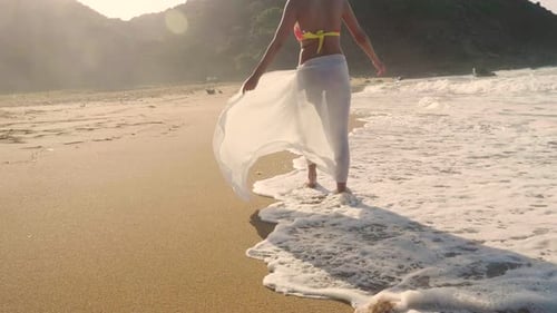 Aerial view of a woman who runs, dances, and has fun on a beautiful white beach and around her a c