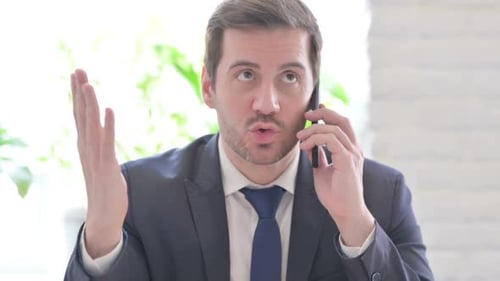 Angry Young Businessman Talking on Phone in Office