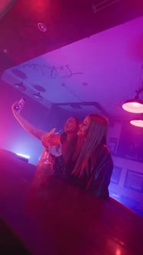 Two Happy Women in a Night Bar Take a Selfie on the Phone in Neon Lighting