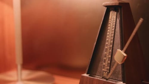 Dusty metronome that is moving back and forth on a lamp lit shelf.