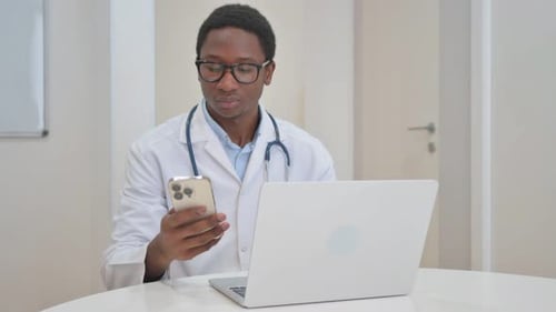 African American Doctor Using Phone and Laptop in Clinic
