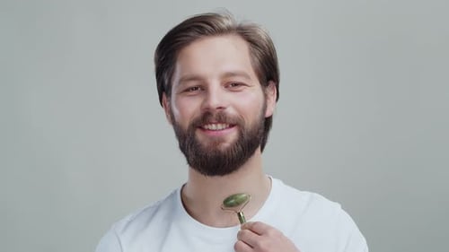 Bearded Handsome Male Model Massaging His Face with Green Jade Roller Beauty Tool for Gentle