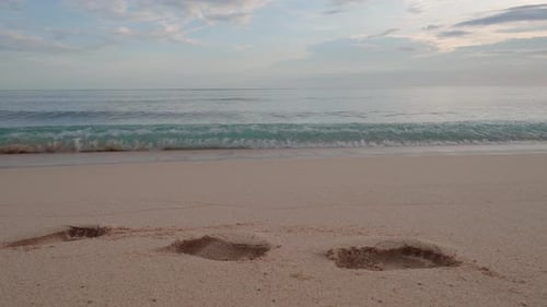 Footprints on White Sand Beach with Slow Motion Ocean Waves at Sunset