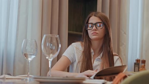 Woman Reviews Wine Options Young Woman Examines Menu and Drinks Water Fashionable Woman Surveys Menu