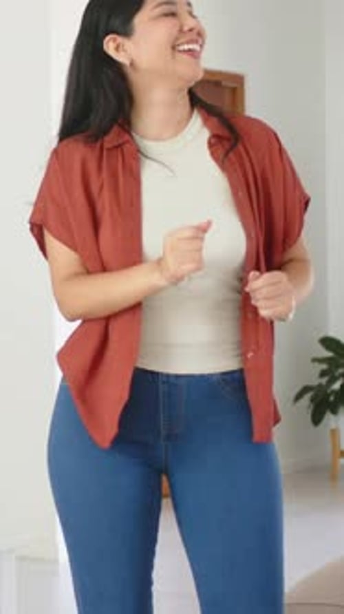 Vidéo verticale : Femme riant dansant directement dans un salon lumineux, portant une chemise rouille, un miroir