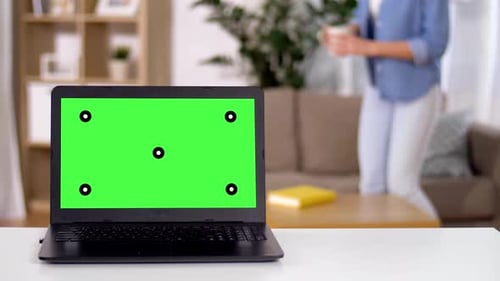 Woman reads book at home while laptop with green screen rests on table