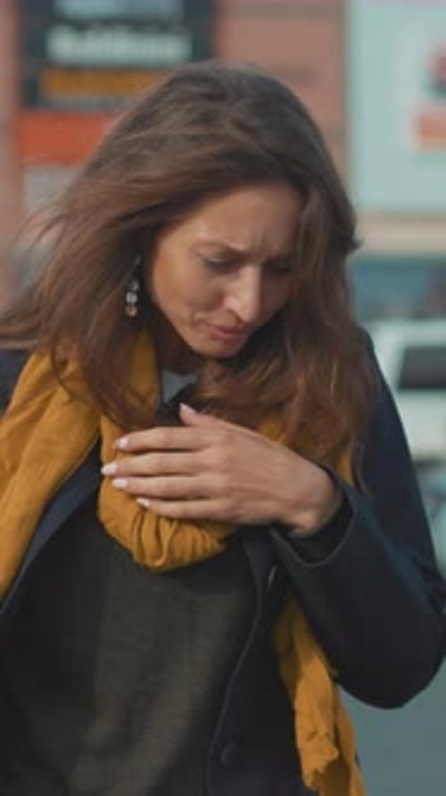 Woman Coughing into Hand in Urban Setting