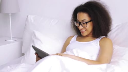 Smiling woman in bed using a tablet
